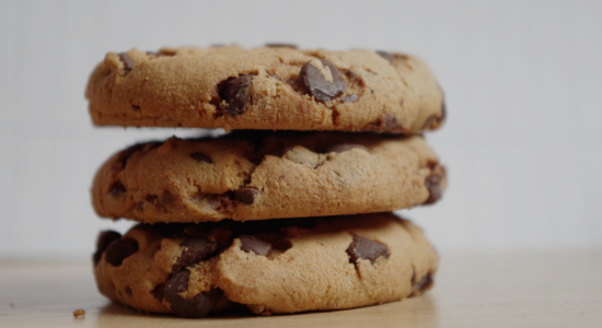 A stack of three chocolate chip cookies on a desk.