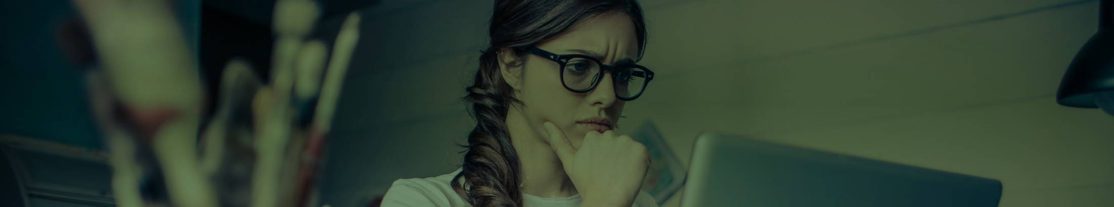 A woman sat at her computer with her hand raised to her chin in deep thought