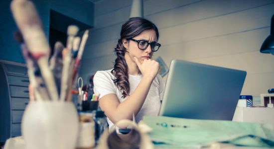 A woman sat at her computer with her hand raised to her chin in deep thought