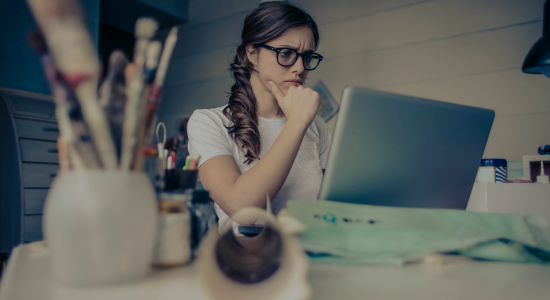 A woman sat at her computer with her hand raised to her chin in deep thought